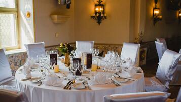 A round dining table set for a formal event with white tablecloths, silverware, and glassware.