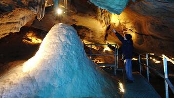 A person standing on a metal staircase inside a cave with stalactites and a large ice formation.