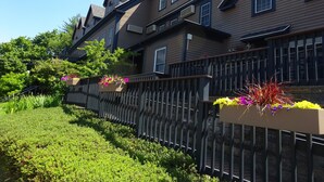 A two-story house with a dark brown exterior, multiple windows, and a black metal fence with flower planters. - Sea Rose Suites (Ogunquit)