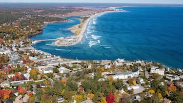 Vista aérea de un pueblo costero con playa, casas y un puente que une la tierra con el agua.
