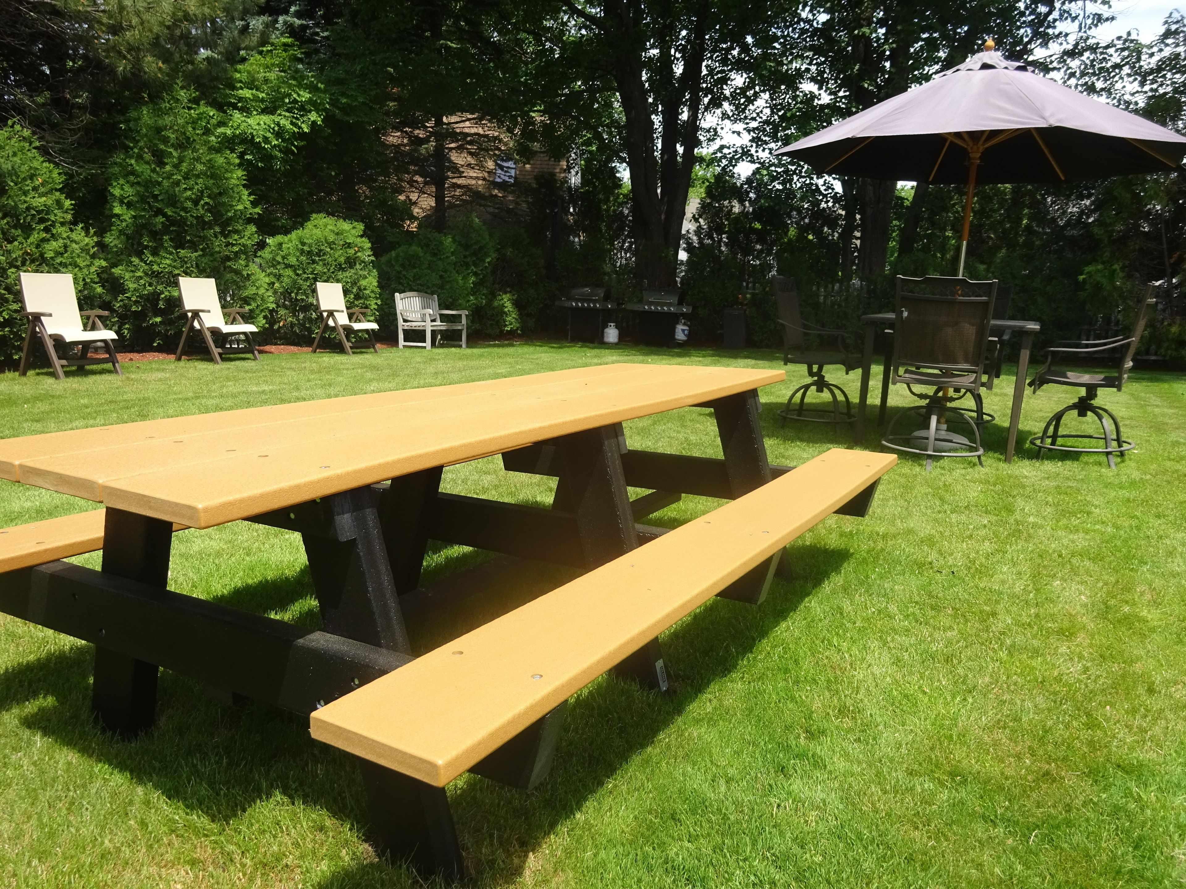 A picnic table with benches in a grassy outdoor area with chairs and a gazebo.