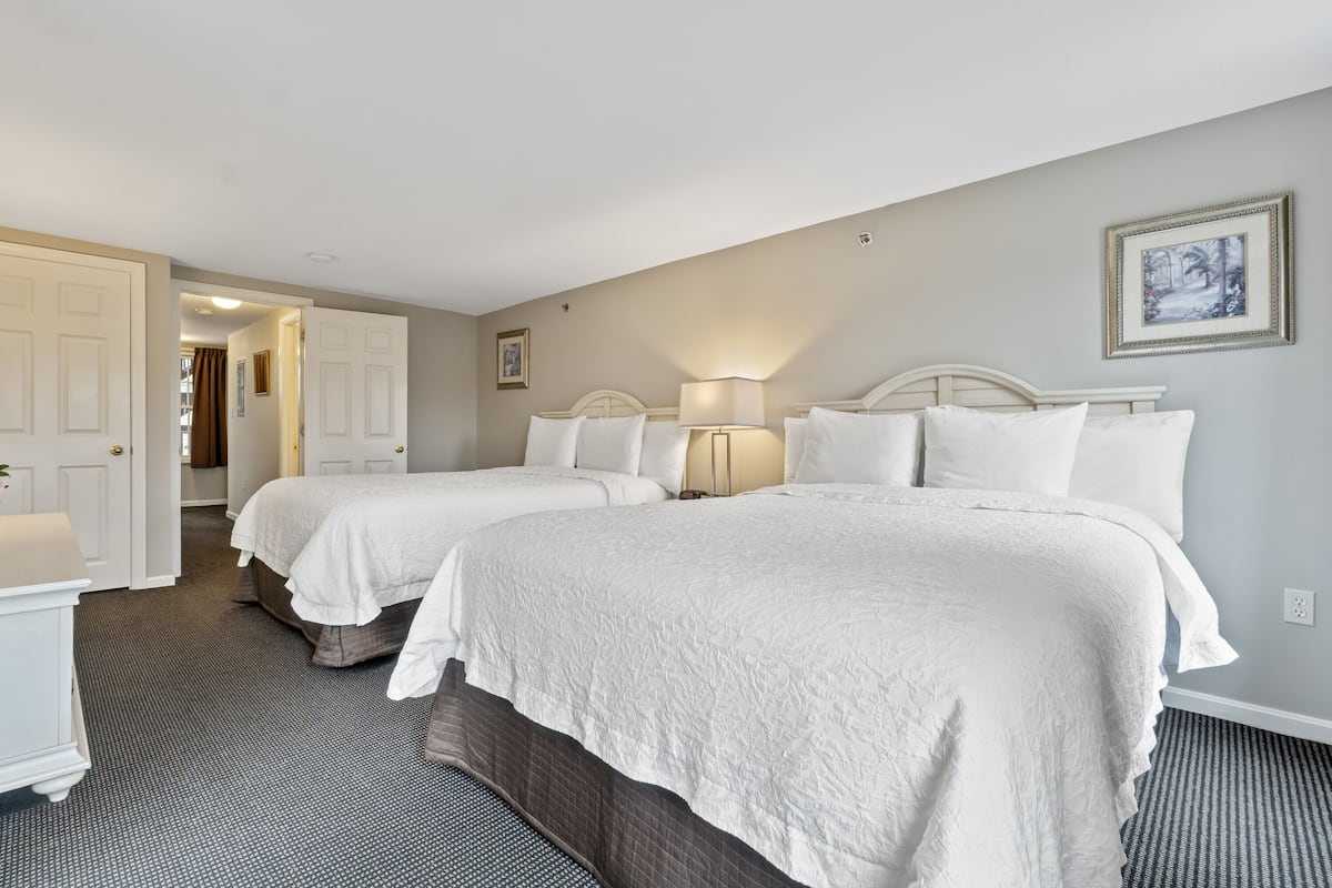A hotel room with two beds, a bathroom, and a hallway.