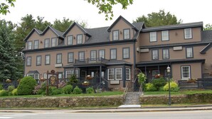 A two-story building with a traditional architectural style, featuring a stone foundation, multiple windows, and a front porch with steps leading to the entrance. - Sea Rose Suites (Ogunquit)