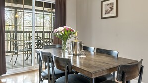 A dining area with a wooden table, chairs, a vase with flowers, and a framed picture on the wall. - Sea Rose Suites (Ogunquit)