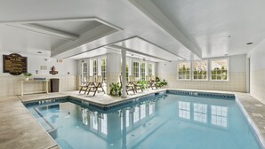 An indoor swimming pool with clear water, surrounded by white walls and large windows. - Sea Rose Suites (Ogunquit)