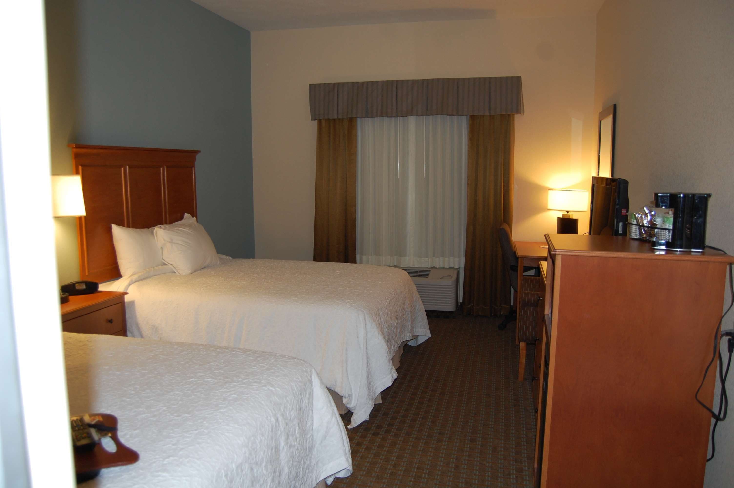 A hotel room with two beds, a desk, a chair, a lamp, and a television.