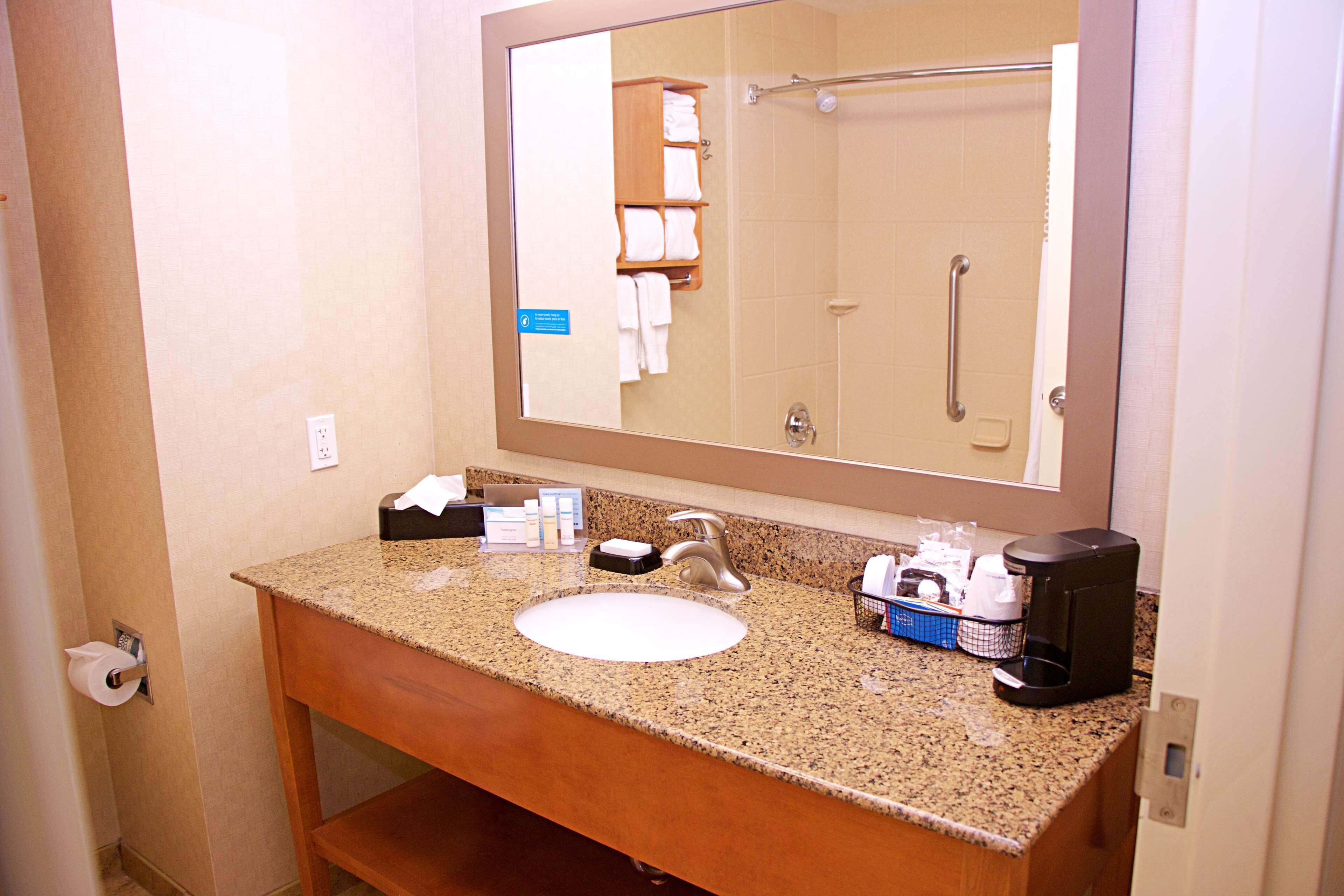 A bathroom with a granite countertop sink, a mirror, a towel rack, and a coffee maker.