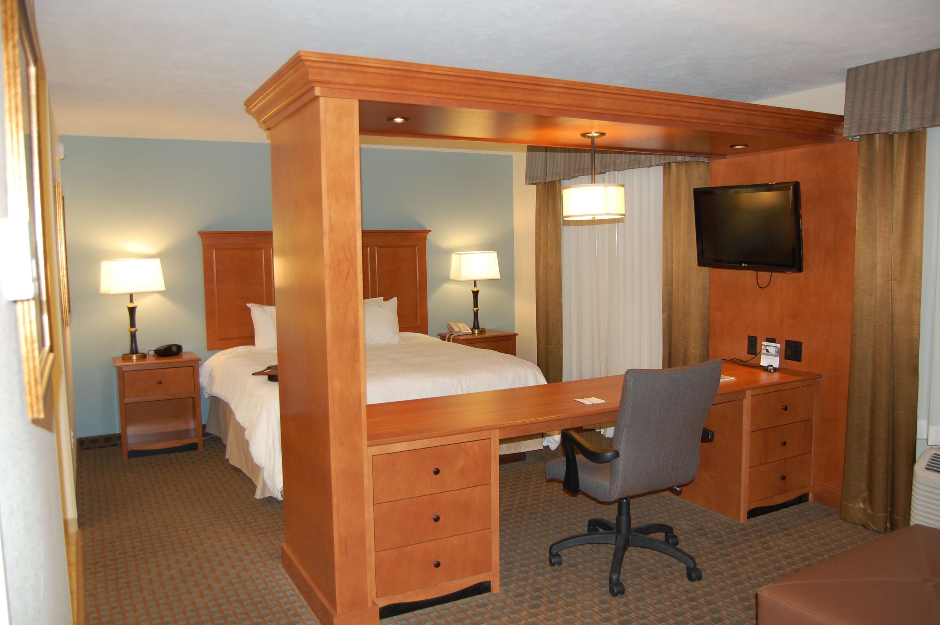 Habitación de hotel con cama con dosel, escritorio con silla, televisión y mesita de noche con lámpara.