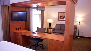 A hotel room with a bed, a desk with a chair, a television, two lamps, and a framed picture on the wall.