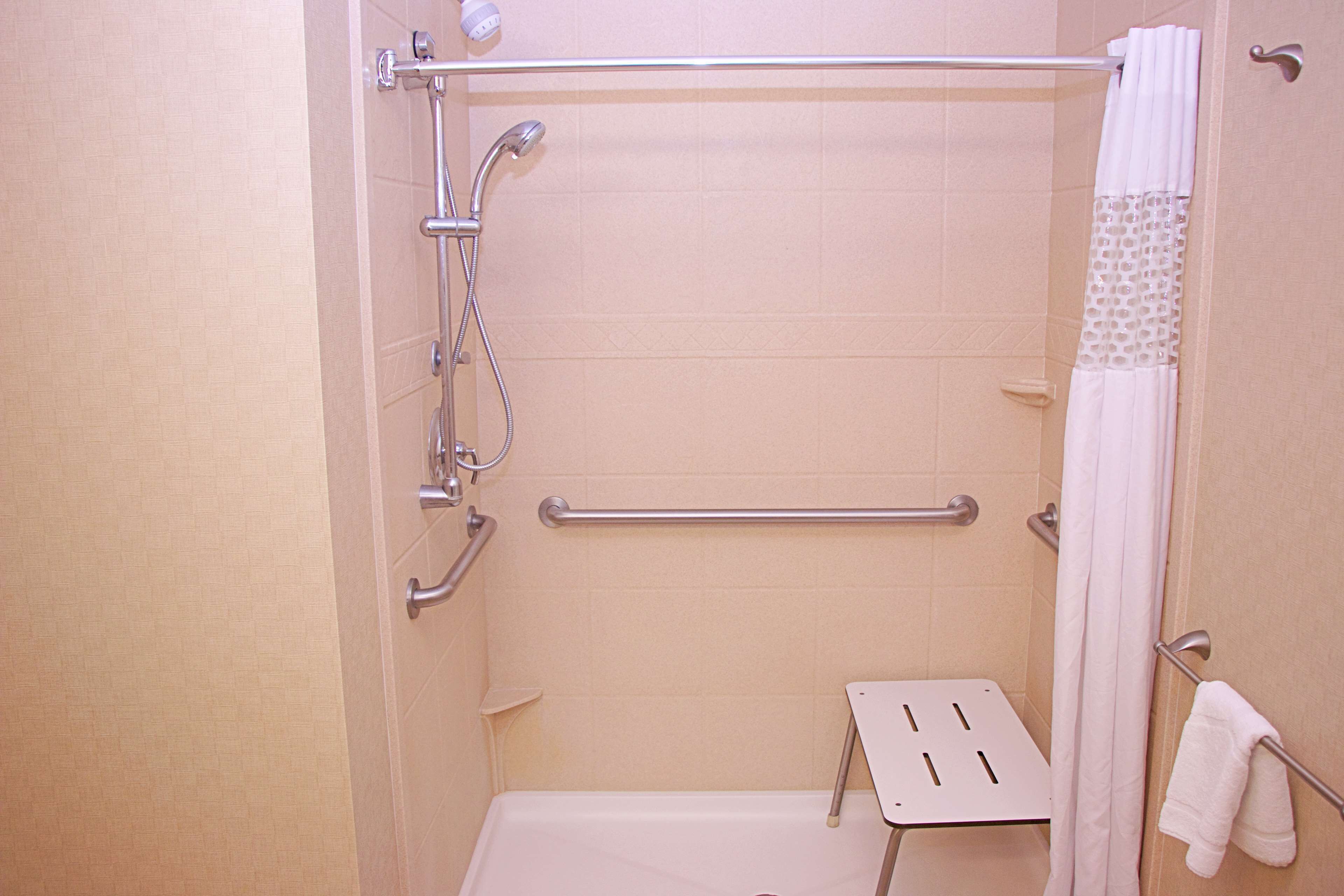 A shower with a grab bar, a white towel rack, and a shower curtain.
