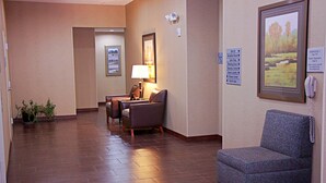 A hotel lobby with a reception desk, a waiting area with chairs, a framed picture on the wall, and a sign listing amenities.