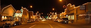 A street lined with buildings, including a theater and a flower shop, with cars parked along the road.