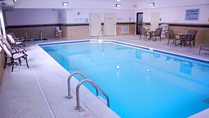 An indoor swimming pool with lounge chairs and tables, a lifeguard chair, and a sign indicating no diving.