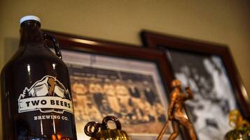 A dark bottle labeled "Two Beers Brewing Co." on a shelf with a framed picture and a golden statue in the background.