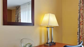 Habitación de hotel con un escritorio de madera, una silla, una lámpara, un espejo y una ventana con cortinas.