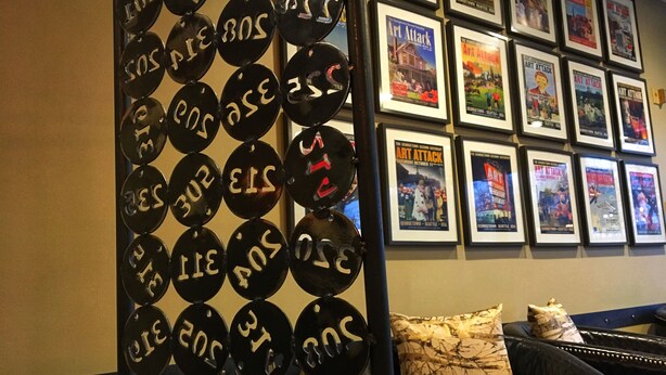 A wall with framed posters and a decorative metal panel with numbers. - Georgetown Inn (Seattle)