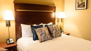 A hotel room with a large bed, two bedside lamps, a nightstand with a phone, and a poster on the wall. - Georgetown Inn (Seattle)
