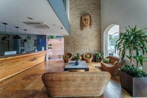 Eine Empfangshalle mit Rezeption, Korbmöbeln, einer großen Pflanze und einer Steinwand mit einer Holzskulptur des Kopfes.