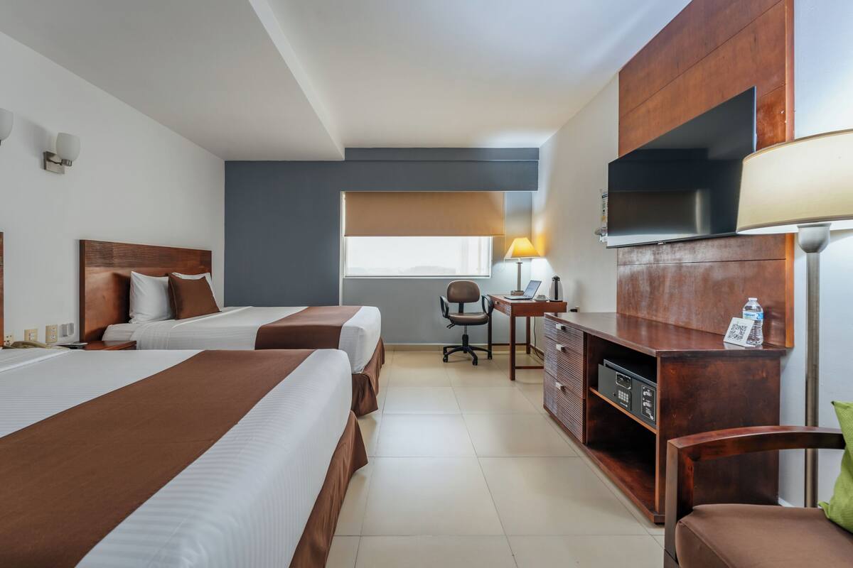 Ein Hotelzimmer mit zwei Betten, einem Schreibtisch, einem Sessel, einem Fernseher und einer Minibar.