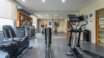 Una palestra con diverse attrezzature per l'allenamento, tra cui tapis roulant e macchinari per pesi, e uno specchio a parete.