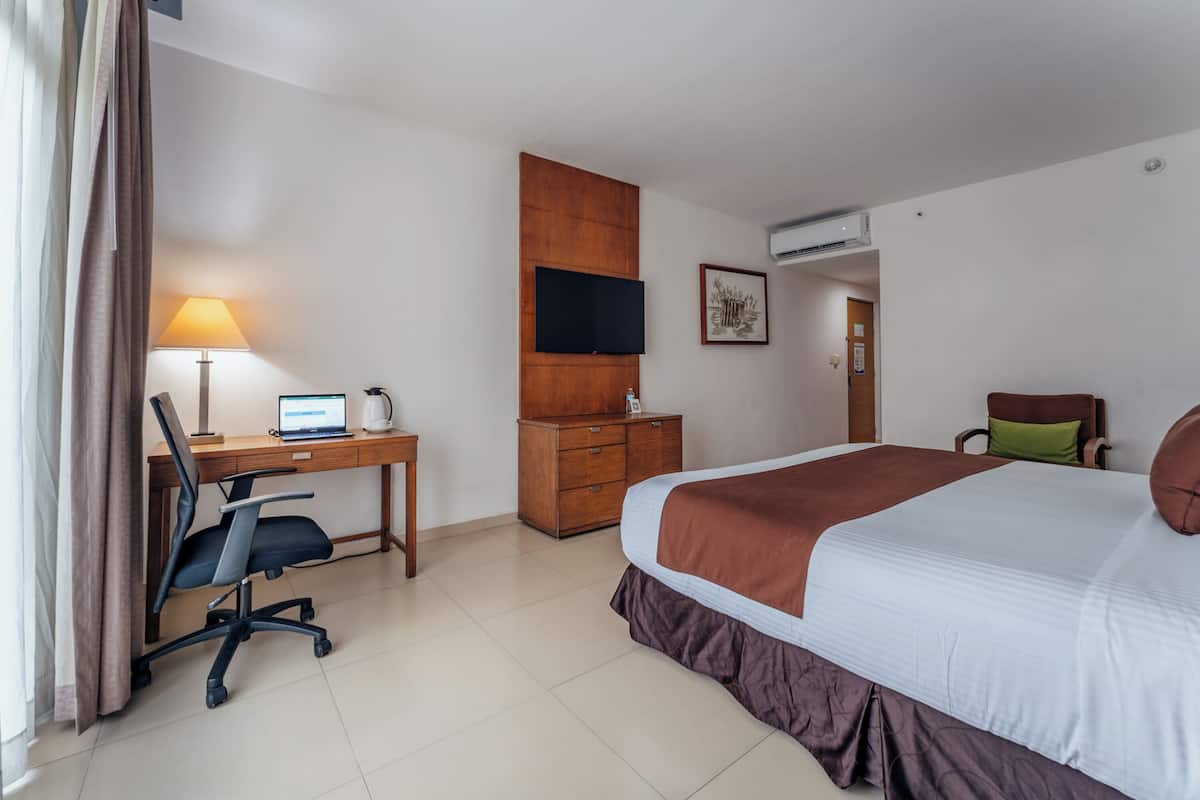 Ein Hotelzimmer mit Bett, Schreibtisch, Stuhl und einem an der Wand befestigten Fernseher.