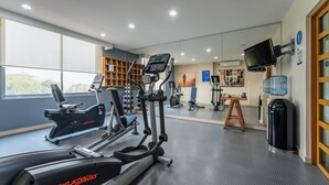 Ein Fitnessraum mit Cardiogeräten, einem Spiegel und einem Wasserkühler.