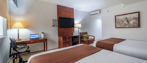 Habitación de hotel con dos camas, un escritorio con una computadora portátil, una silla, un televisor montado en la pared y un cuadro.