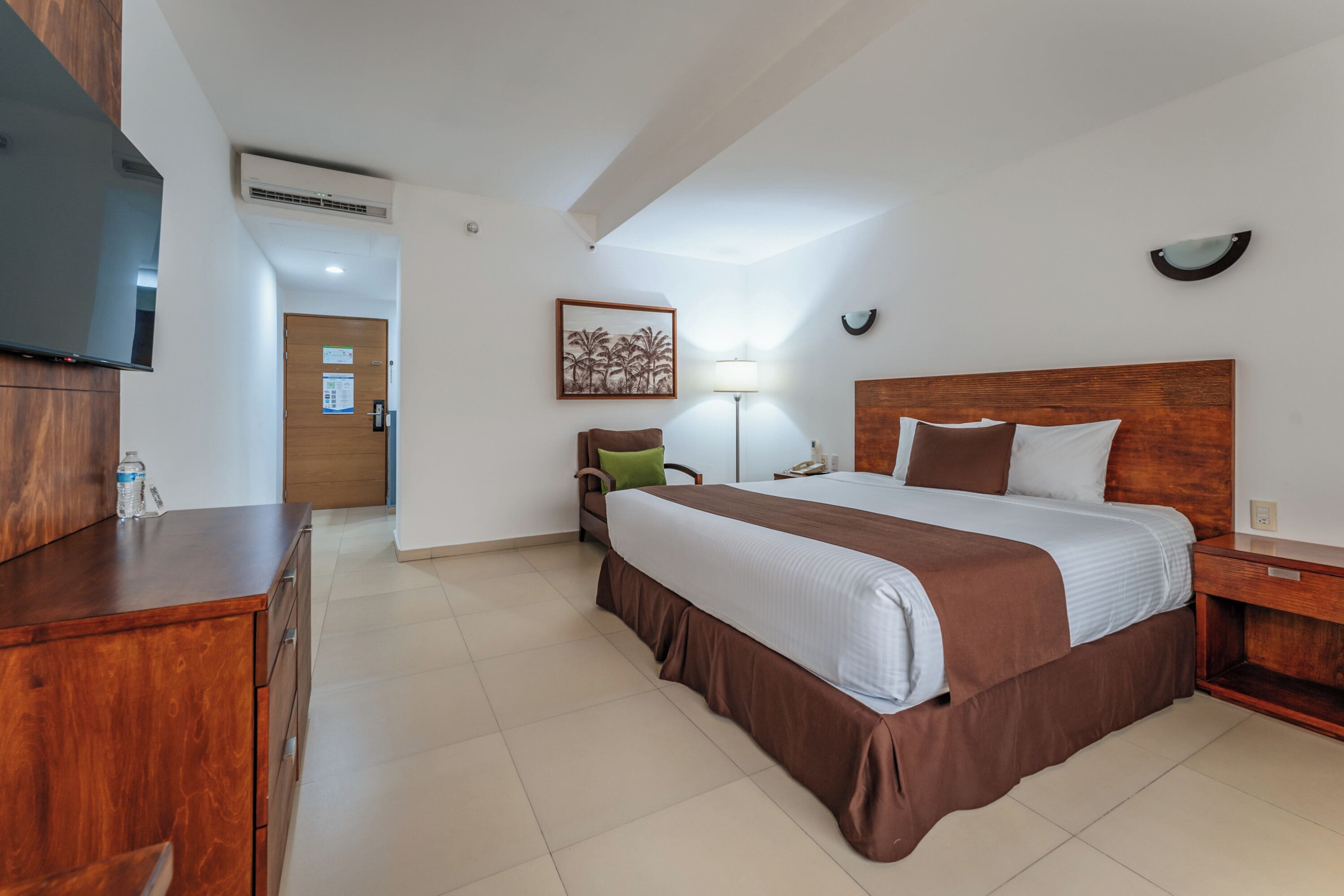 Una habitación de hotel con una cama, un escritorio, una silla, un televisor y una lámpara.