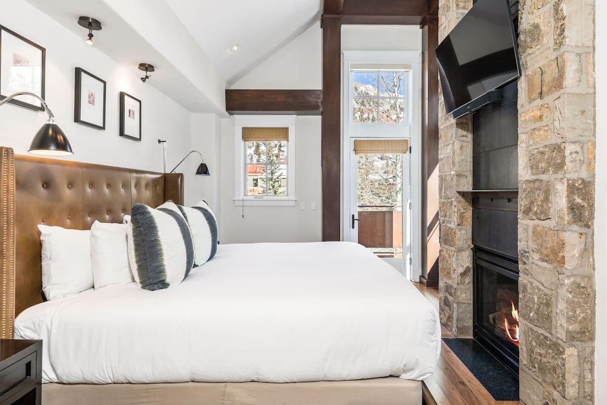 A bedroom with a large bed, a stone fireplace, and framed pictures on the wall.