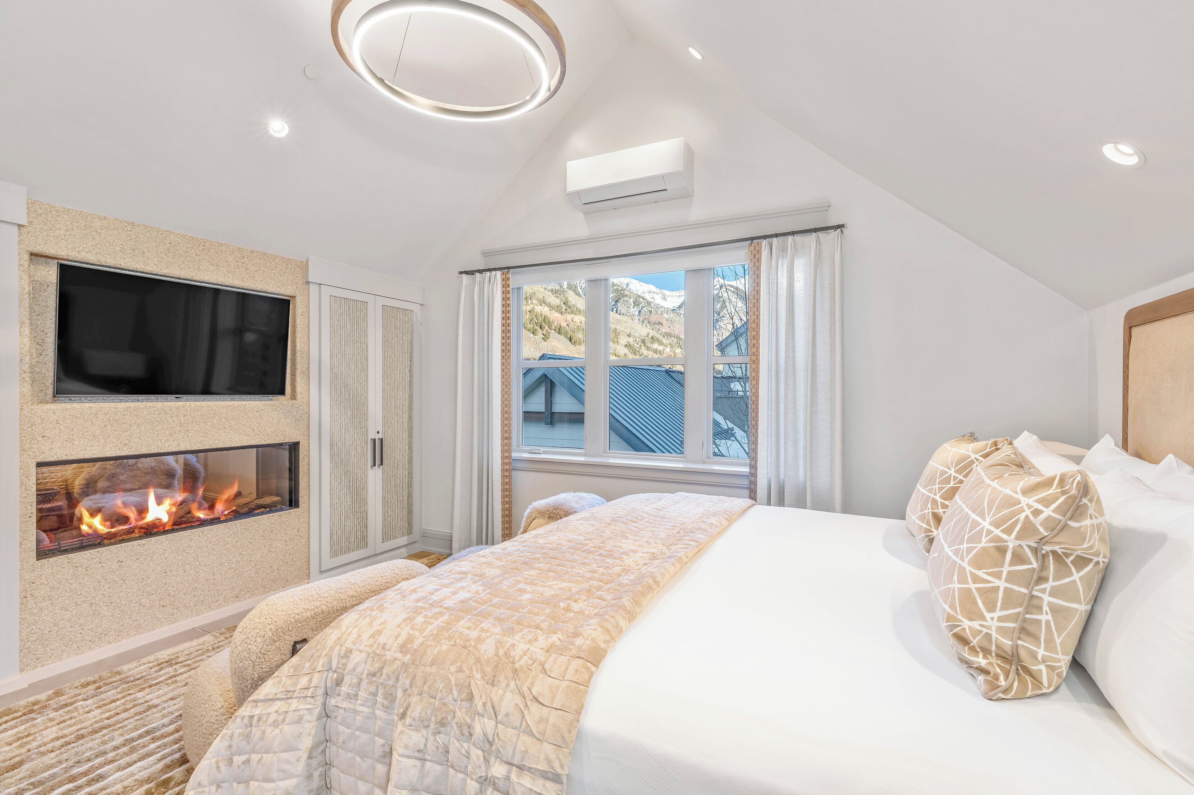 A bedroom with a bed, a fireplace, a TV, and a window with a view of a mountain.