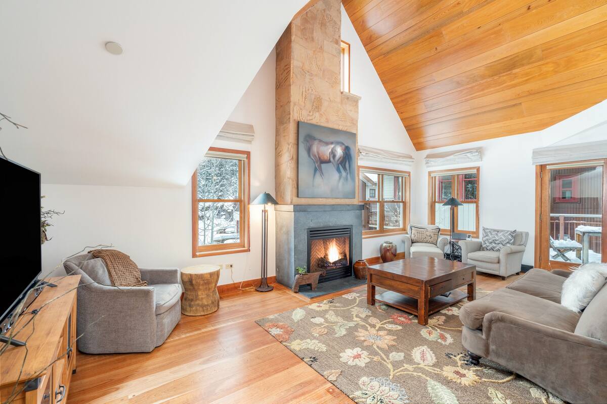 A spacious living room with a fireplace, wooden flooring, and a high ceiling.