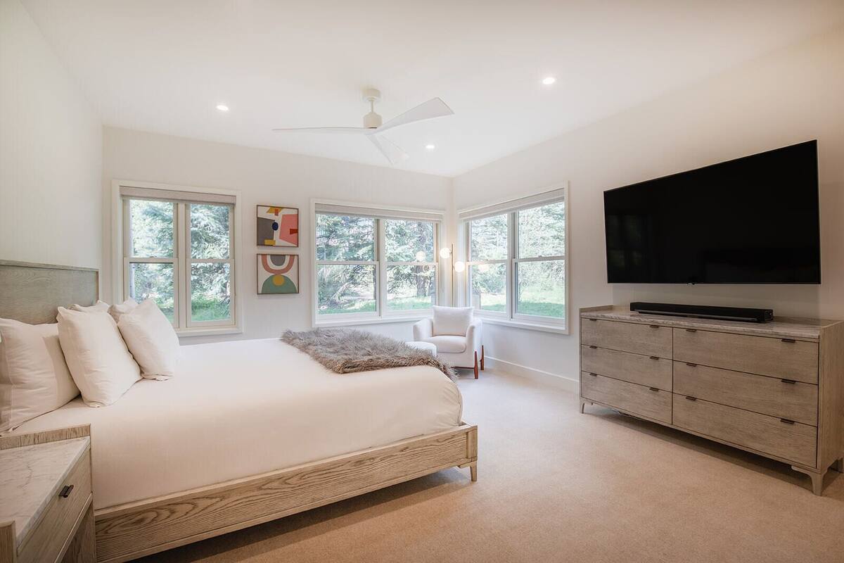 A bedroom with a large bed, a TV, a dresser, and multiple windows.