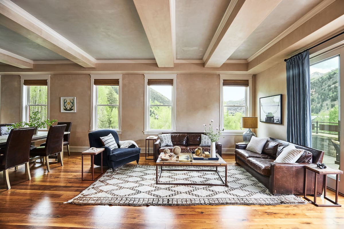 A spacious living room with a wooden floor, a large coffee table, a sofa, and a dining area with chairs and a table.