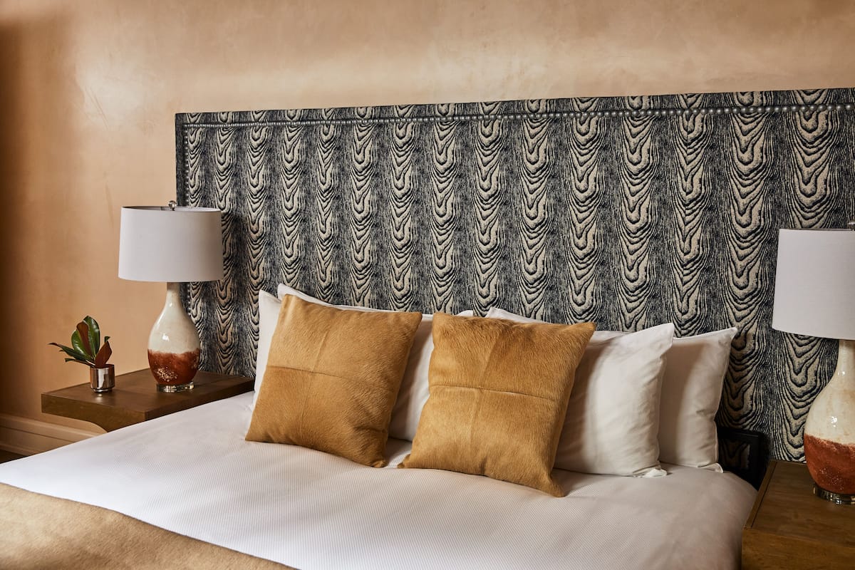 A neatly made bed with two pillows, a patterned headboard, and two bedside tables with lamps and small plants.