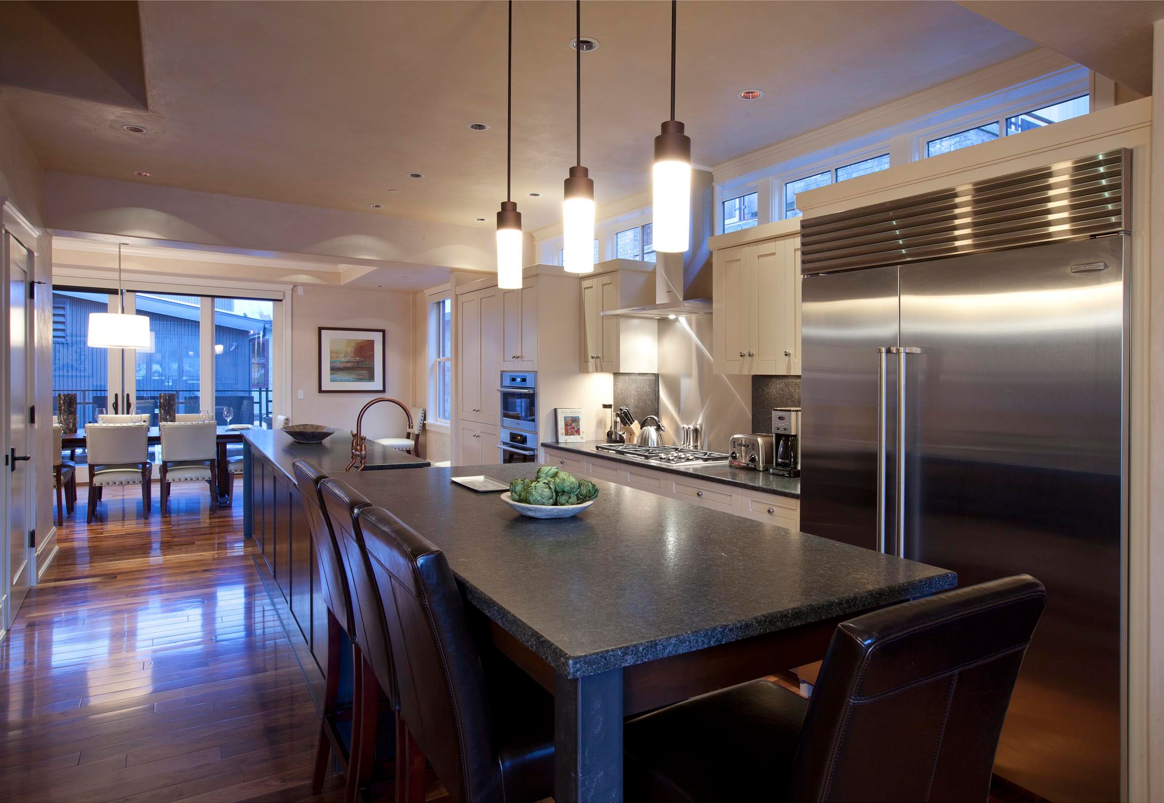 A modern kitchen with a large island, stainless steel appliances, pendant lighting, and a view to the outside.