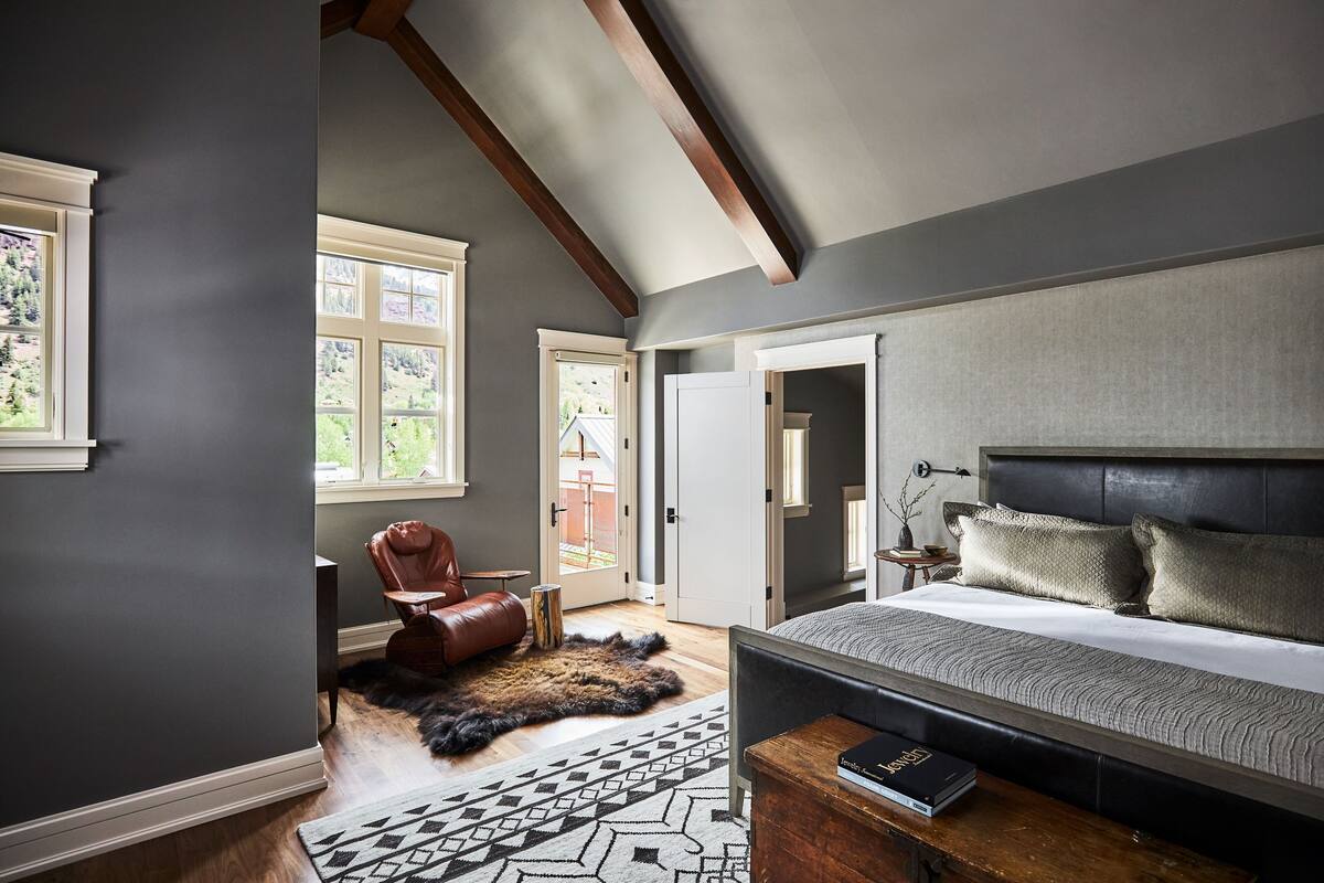 A bedroom with a large bed, a leather chair, a rug, and a view of the outdoors through a window.