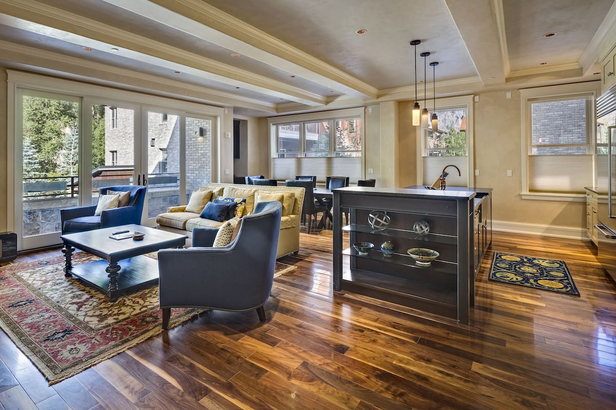A spacious living area with a large window, a dining table, and a kitchen area.