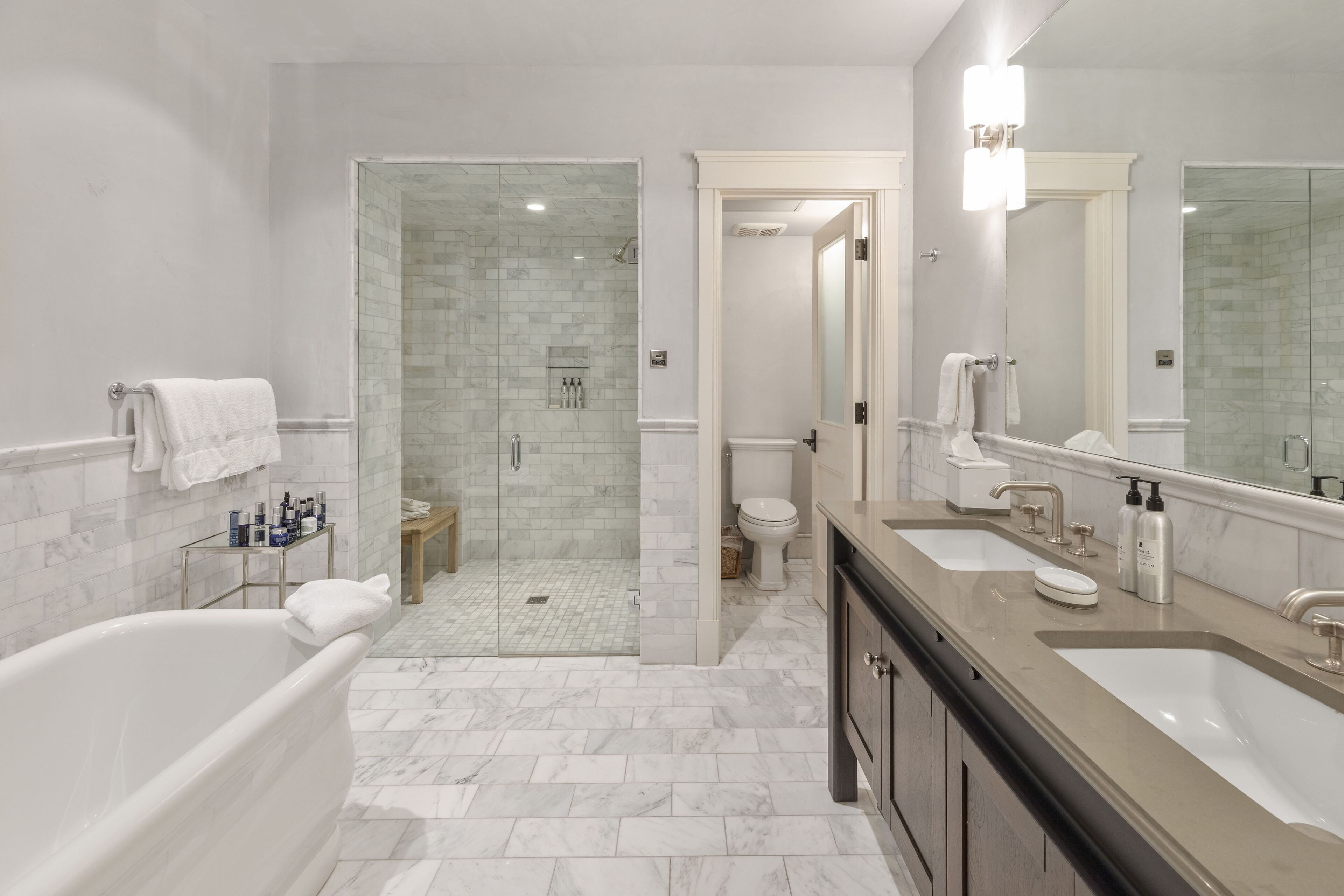 A modern bathroom with a bathtub, two sinks, a glass-enclosed shower, and a toilet.