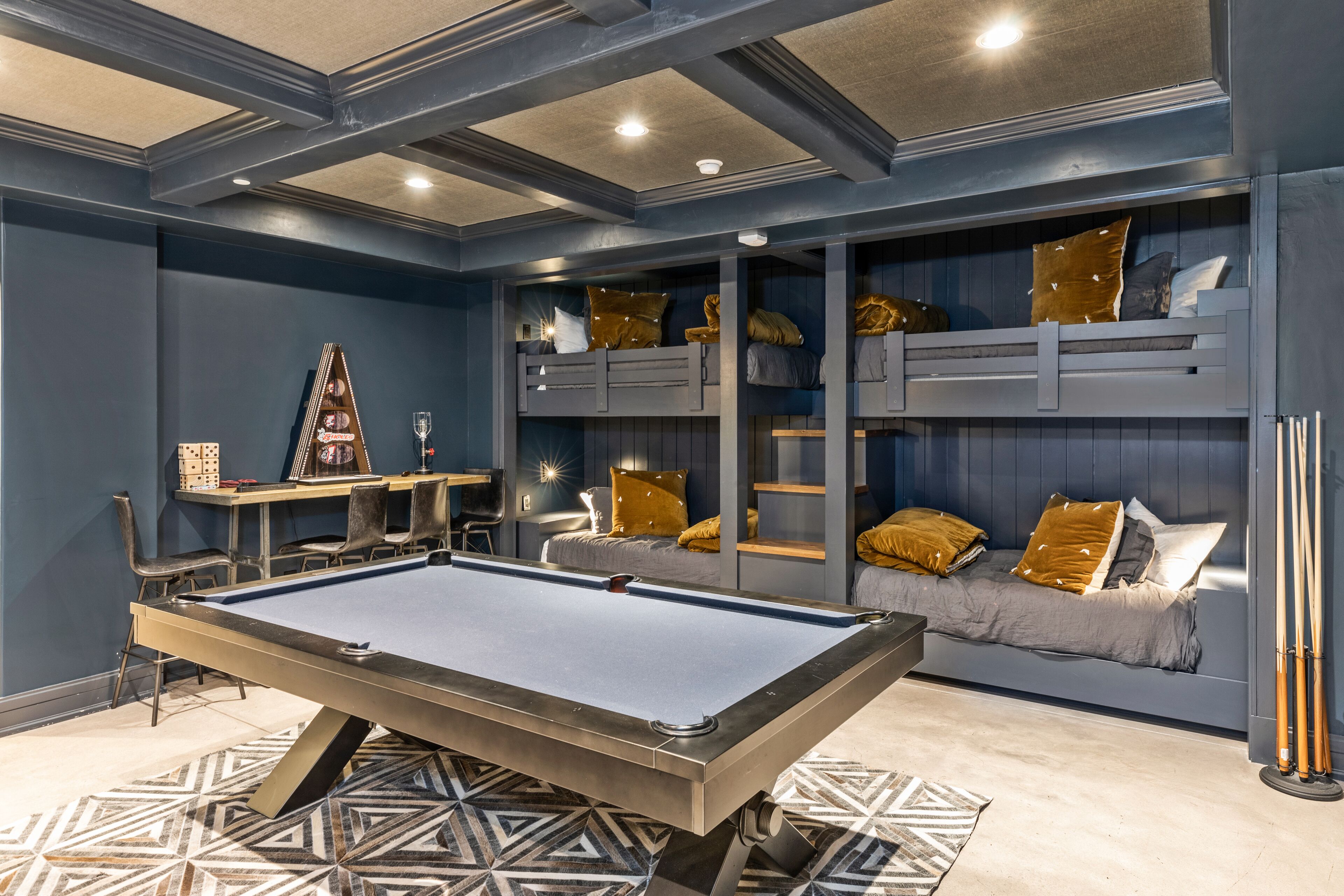A pool table in a room with bunk beds, a guitar, and a billiards cue rack.