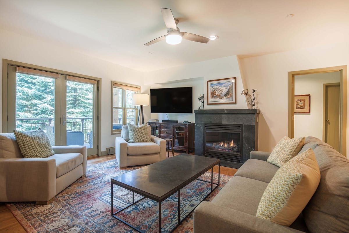 A living room with a fireplace, a television, and a ceiling fan.
