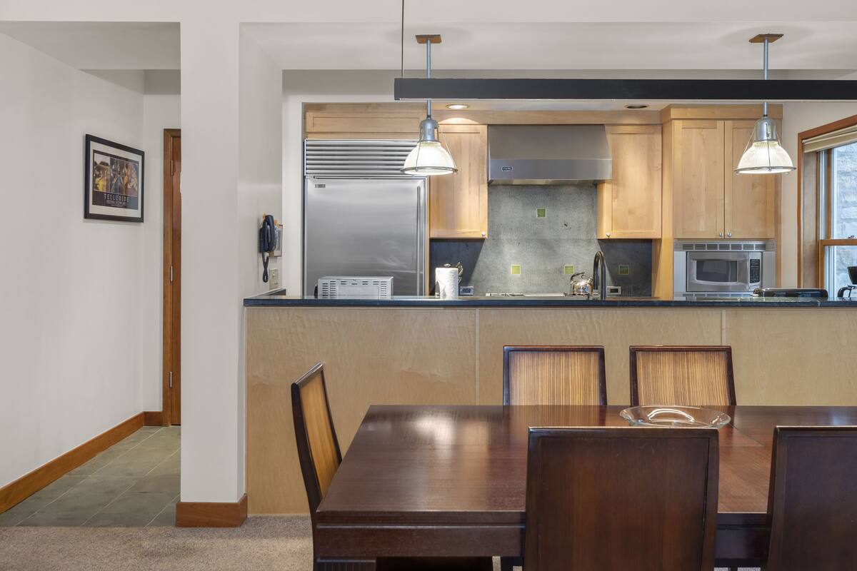 A modern kitchen with wooden cabinets, stainless steel appliances, and pendant lighting.