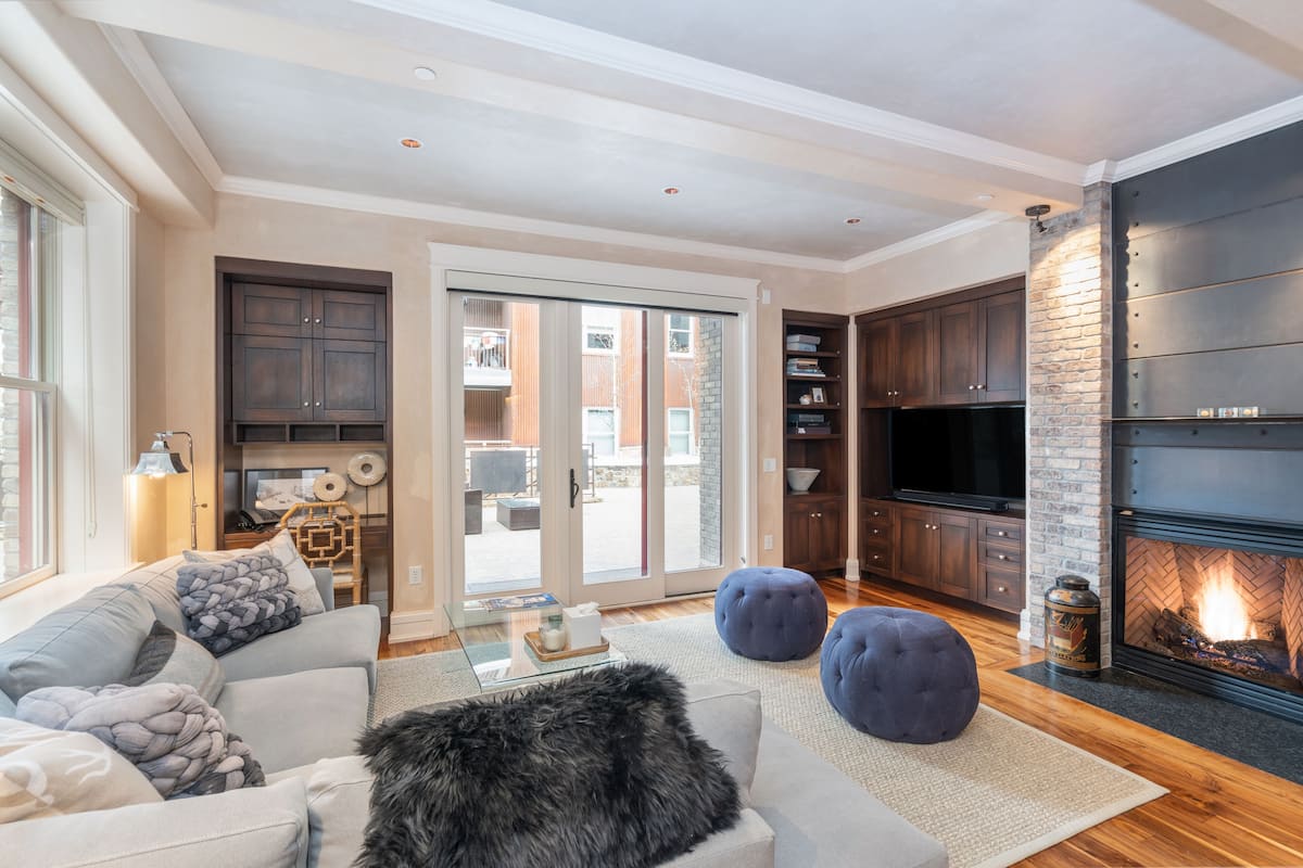 A modern living room with a fireplace, a sofa, ottomans, and a television.