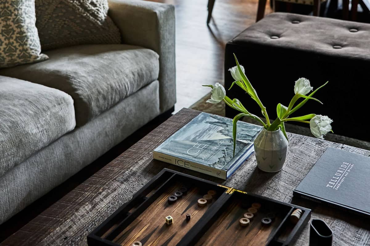 A cozy living room with a sofa, a coffee table with a board game, a vase with flowers, and a book.