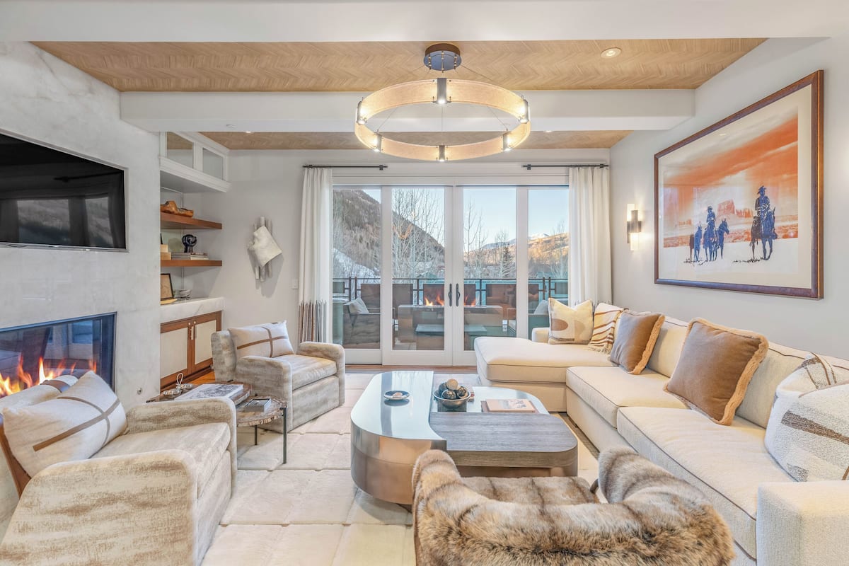 A modern living room with a fireplace, comfortable seating, and a large window overlooking a scenic view.