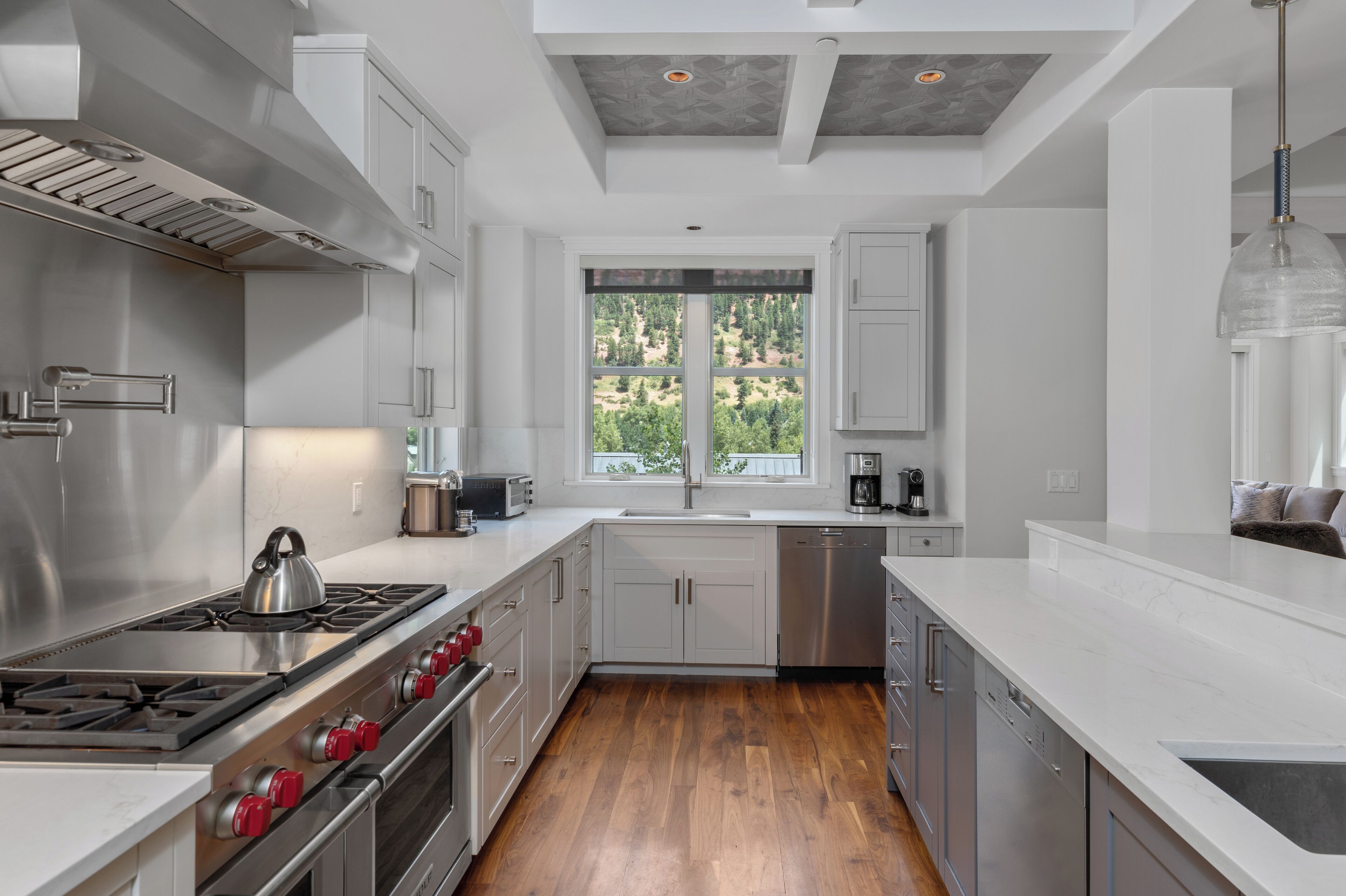 A modern kitchen with stainless steel appliances, white cabinetry, and a large window providing a view of greenery outside.