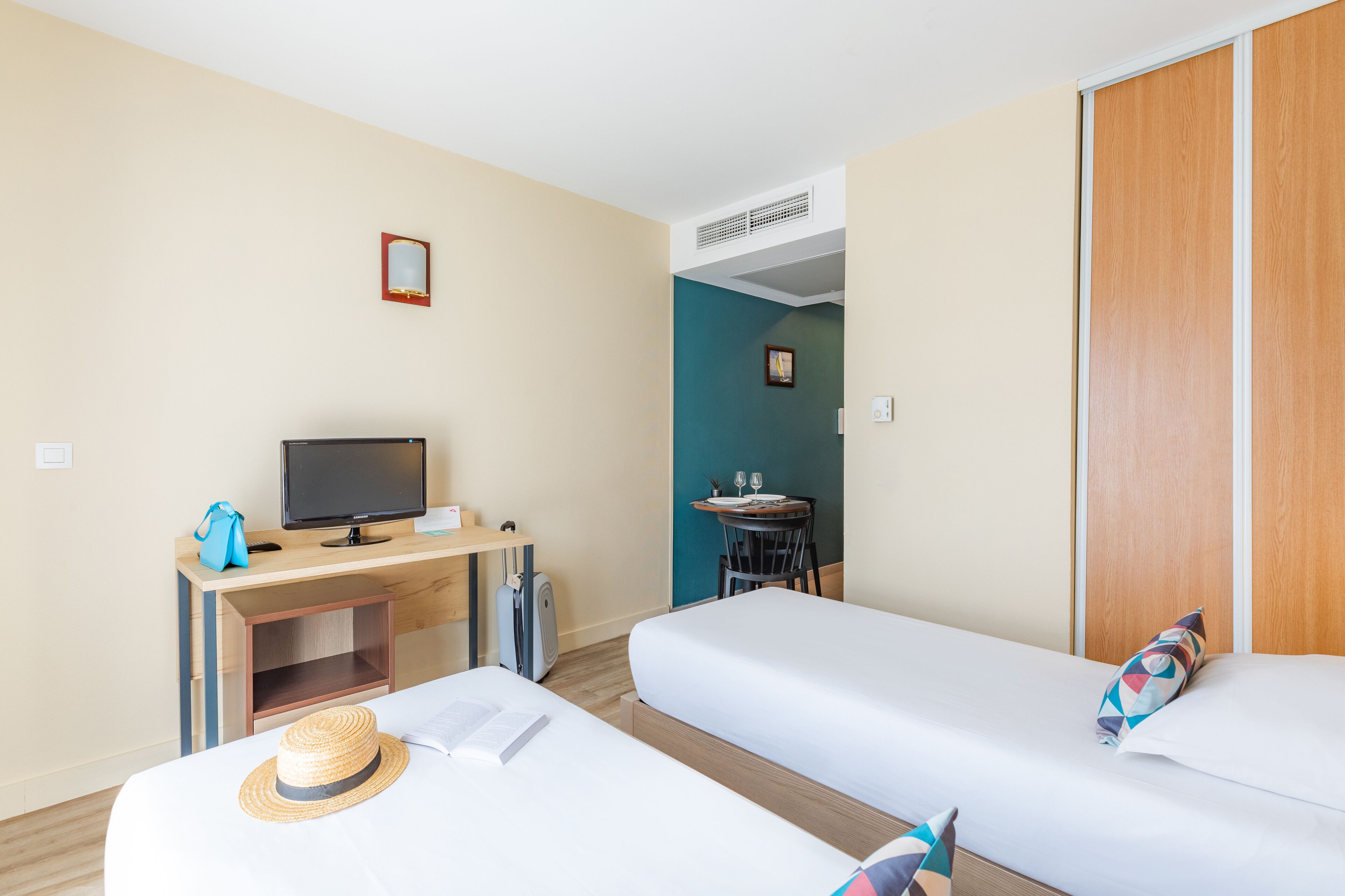 Ett hotellrum med två separata sängar, ett skrivbord med en dator, ett litet bord med en stol och en garderob.