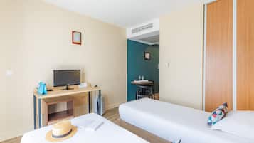 Ett hotellrum med två separata sängar, ett skrivbord med en dator, ett litet bord med en stol och en garderob.