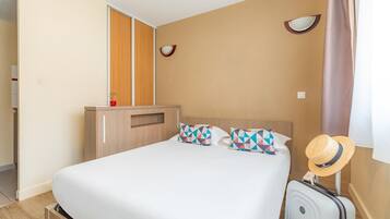 Una habitación de hotel con una cama, un armario, una maleta y un sombrero en la pared.
