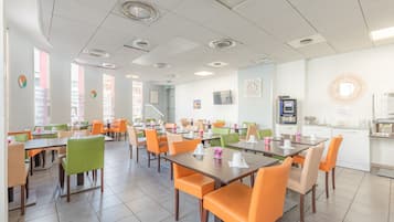 A spacious dining area with multiple tables and chairs, a kitchen area, and a staircase leading to an upper level.