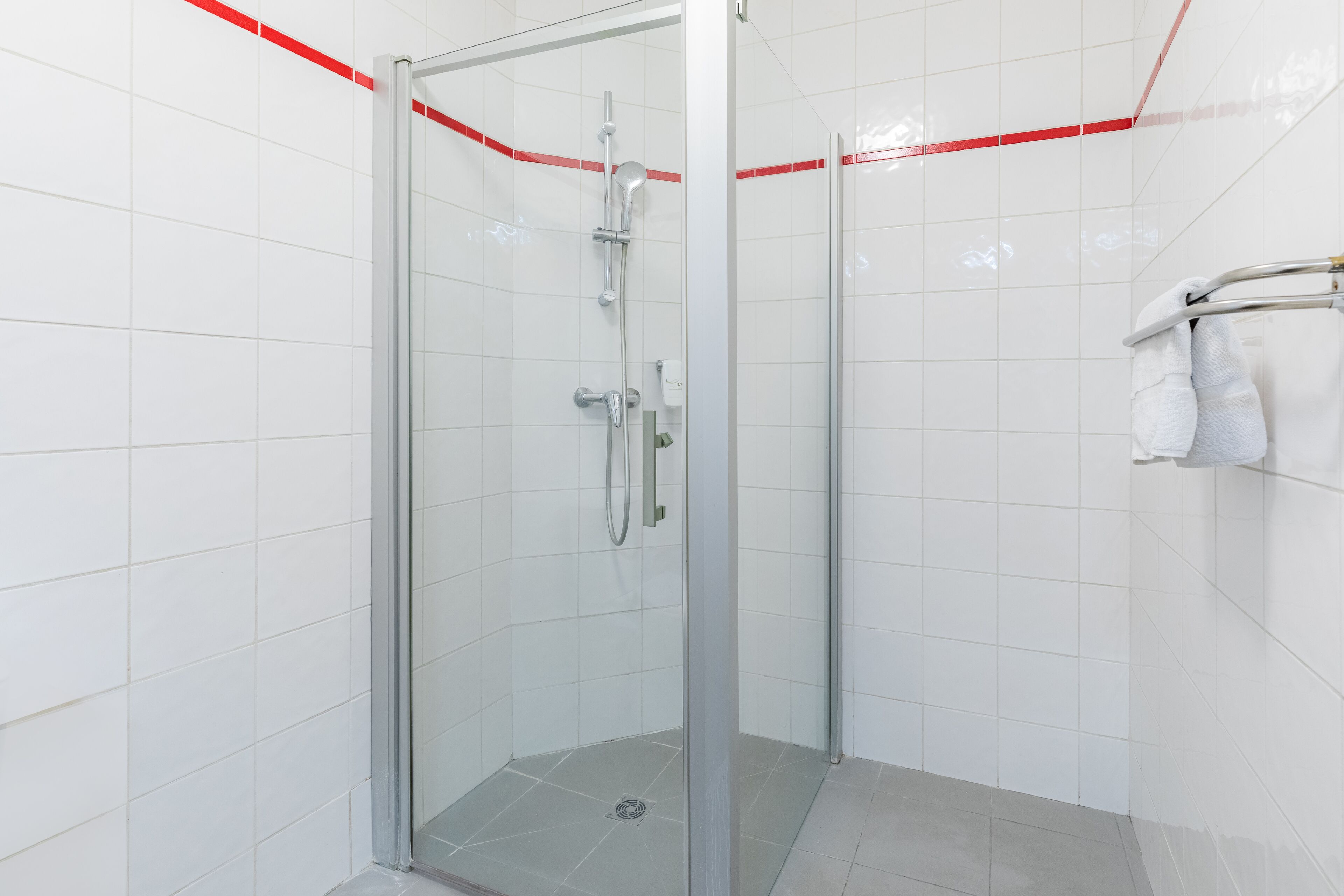 Zona de ducha con mampara de vidrio, cabezal de ducha manual y llave de pared.